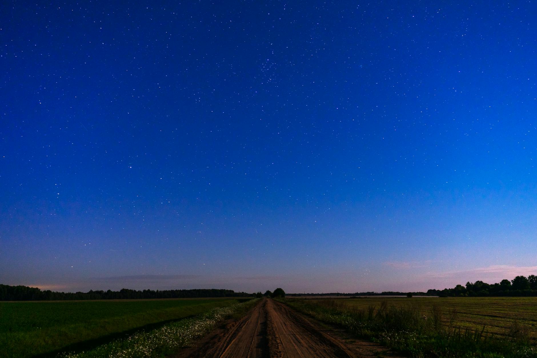 A dirt road cuts through rural Missouri fields under a deep blue twilight sky filled with stars.