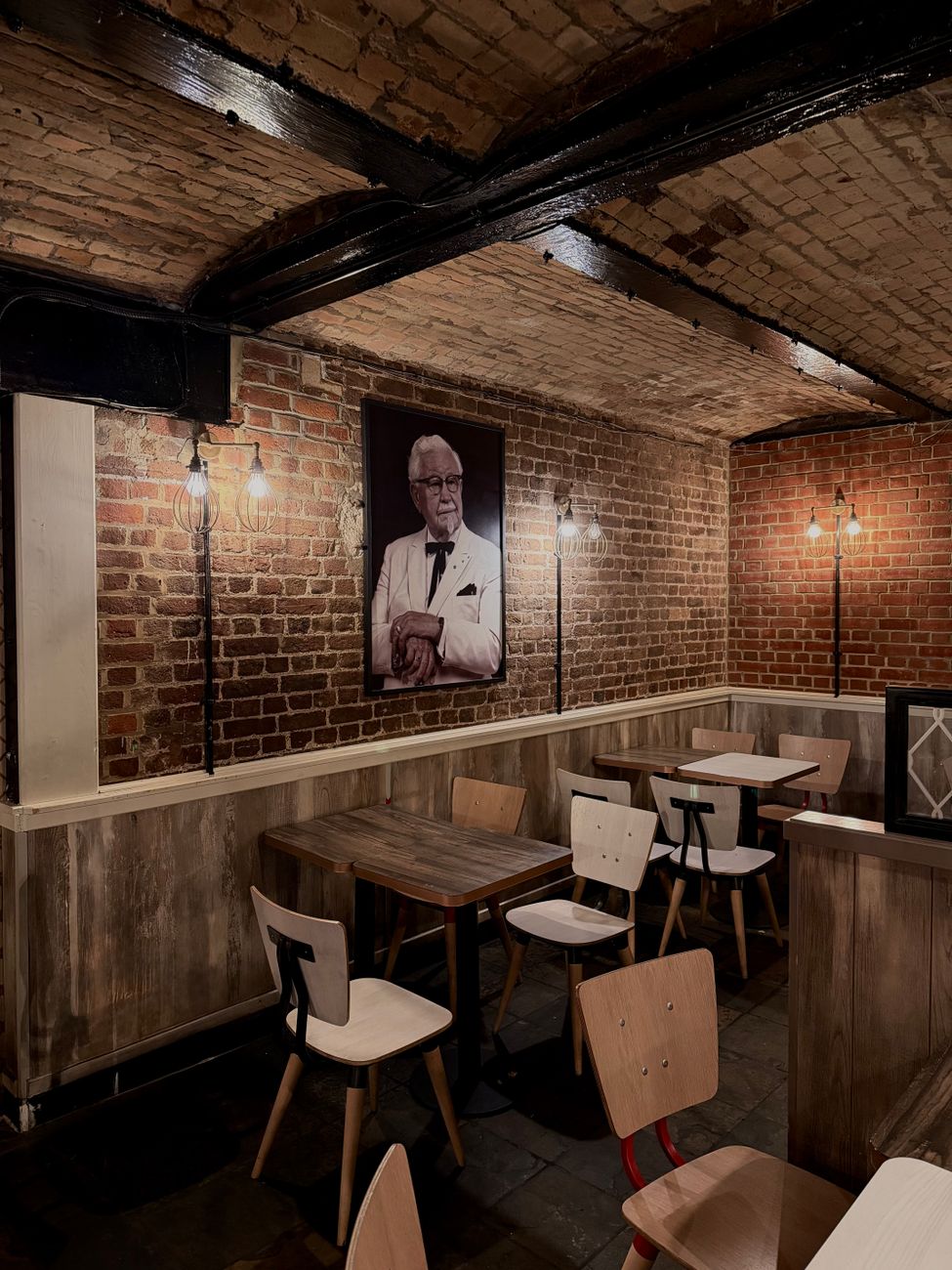 Colonel Sanders portrait hanging on a brick wall inside a KFC restaurant.
