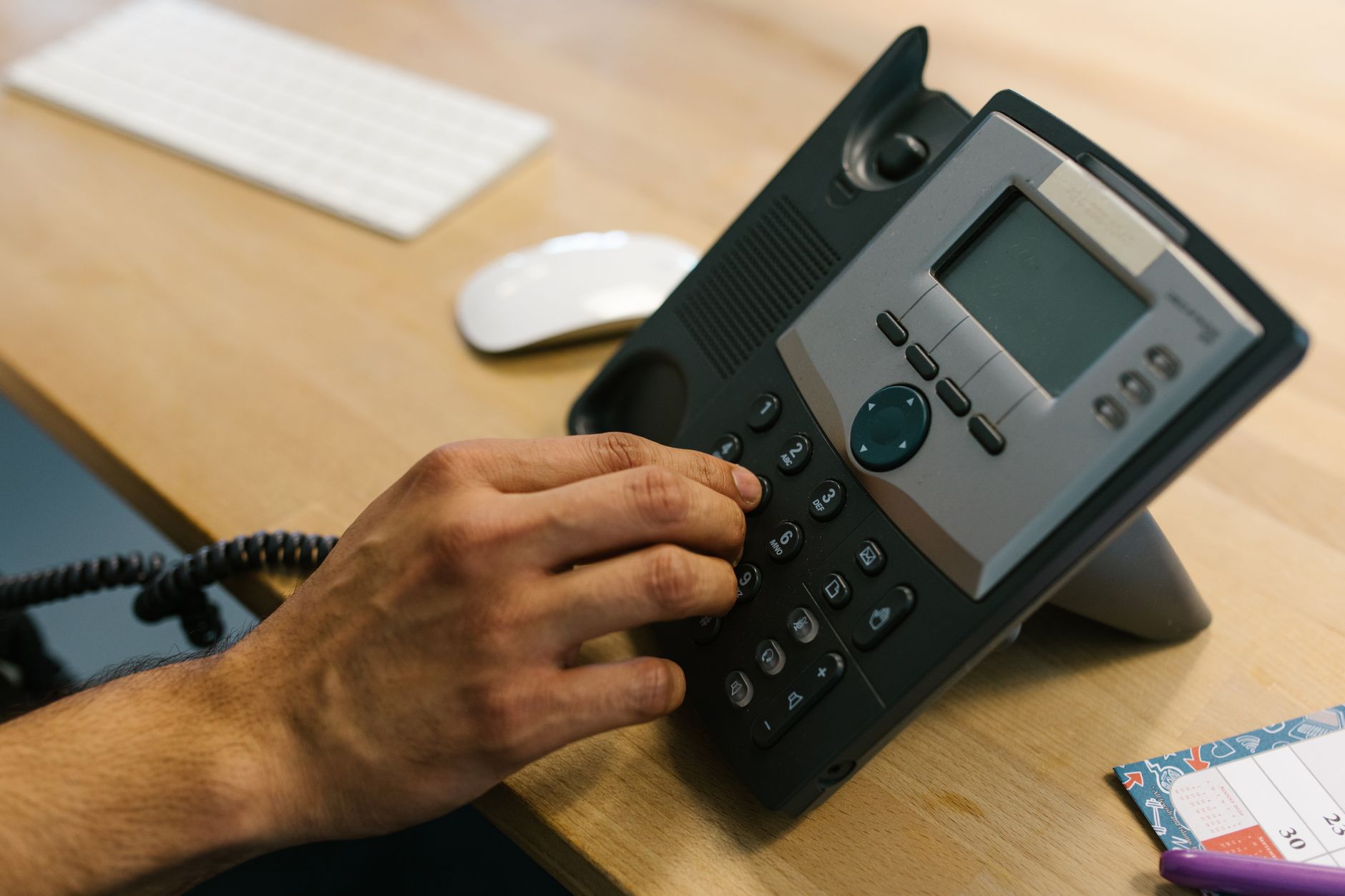A hand reaching for a ringing desk phone.