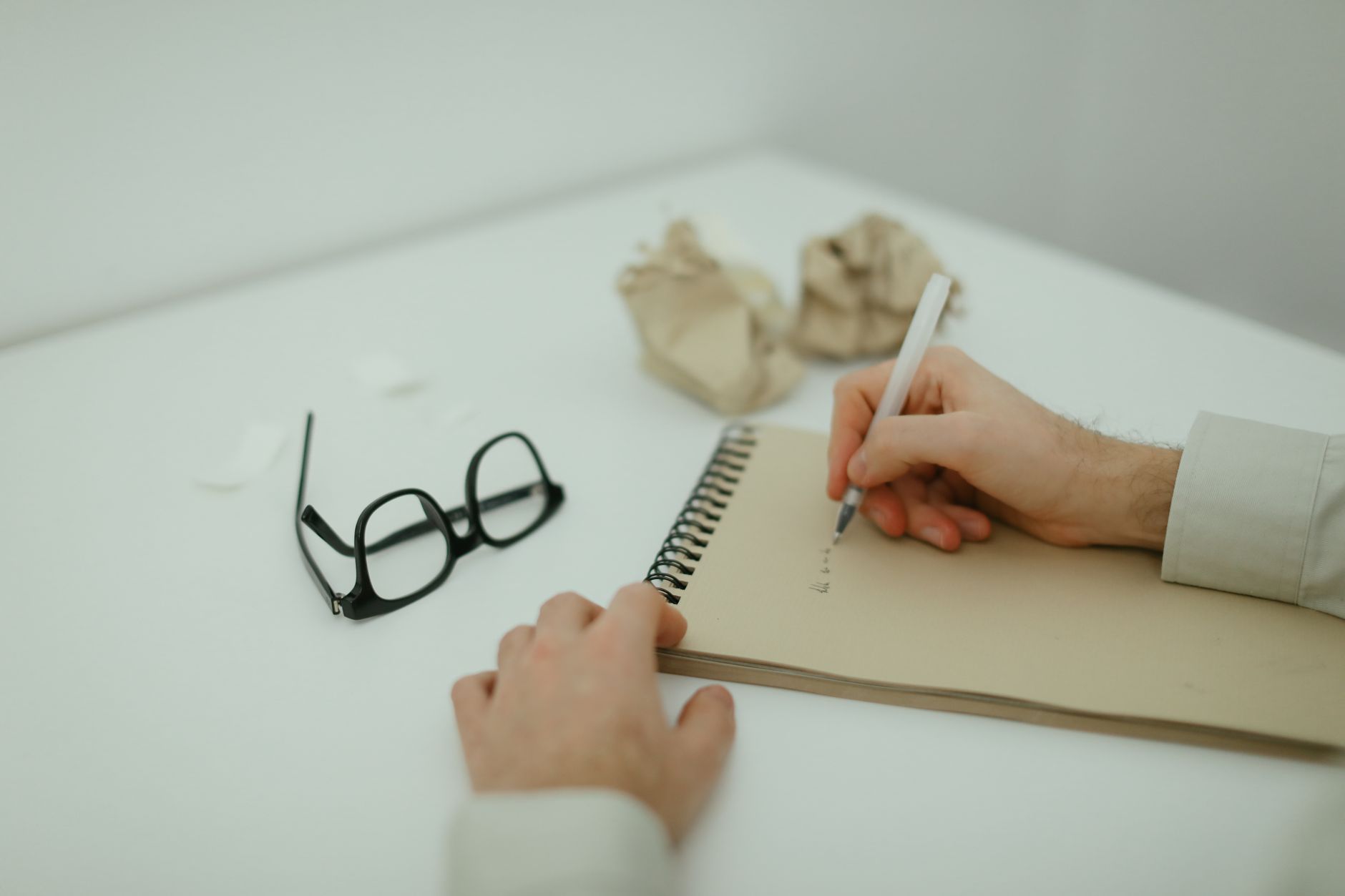 a hand writing on a notepad beside crumpled drafts.